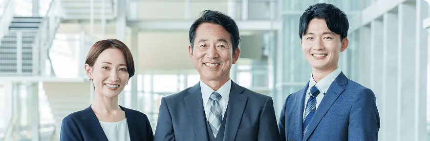 スーツ姿の男女3名が屋内で笑顔を見せる集合写真