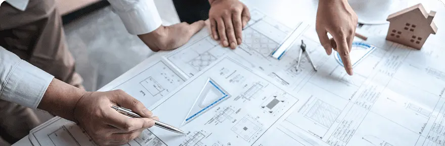 設計図を囲んで3人の手が打ち合わせしている様子