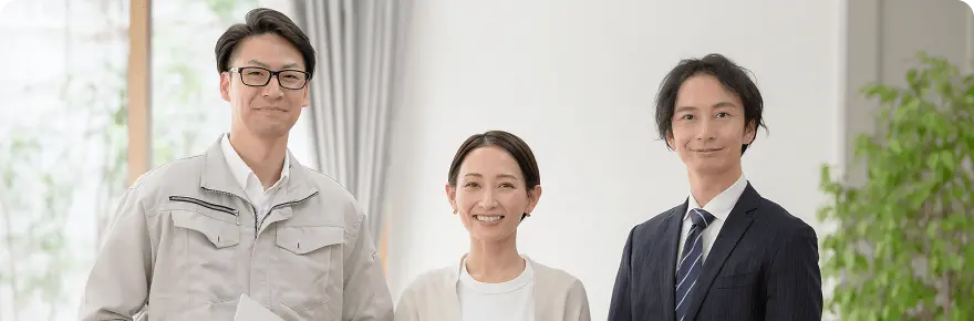 スーツ姿と作業服姿の男性2人とカジュアルな女性が並んで微笑んでいる