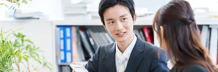 スーツ姿の営業担当者が顧客と相談しながらスマートフォンを見せて説明している場面